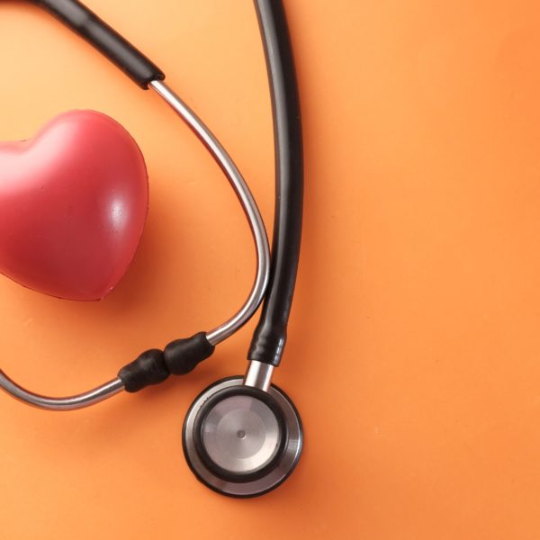 Estetoscopio y corazón rojo sobre fondo naranja, representando la importancia del diagnóstico genético preimplantacional en la reproducción asistida.